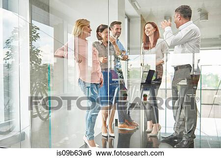 Stock Photograph - View through glass of colleagues standing in office talking. Fotosearch