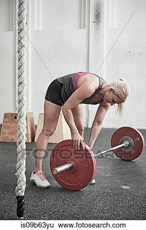 Stock Photograph - Woman adjusting barbell in cross training gym. Fotosearch