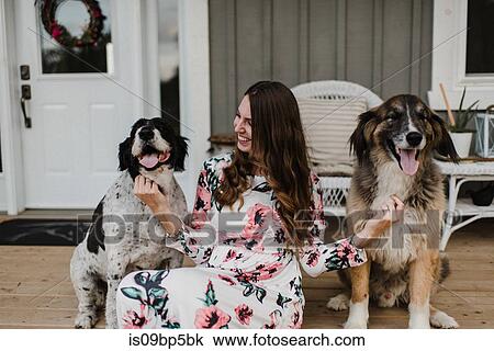 Stock Image - Woman and her two dogs sitting on porch. Fotosearch