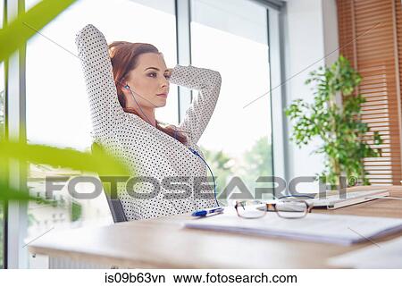 Woman at desk hands behind head looking away View Large Photo Image Picture - Woman at desk hands behind head looking away. Fotosearch