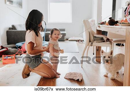 Stock Photo - Woman changing clothes on toddler daughter. Fotosearch