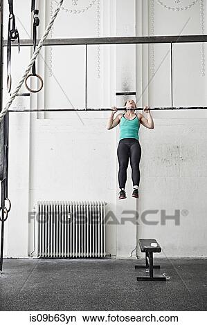 Picture - Woman doing chin-up in cross training gym. Fotosearch