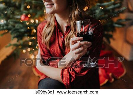 Stock Image - Woman drinking wine beside decorated Christmas tree. Fotosearch