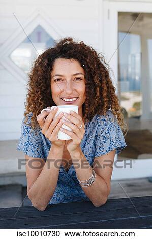 Stock Image - Woman enjoying hot drink clasped in hands at home. Fotosearch