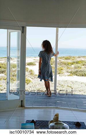 Picture - Woman enjoying view of sea on porch of beach house. Fotosearch