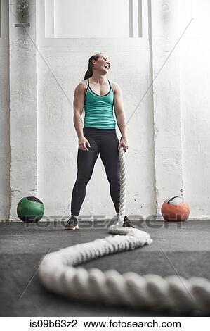 Stock Image - Woman holding battle rope in cross training gym. Fotosearch