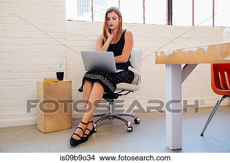 Picture - Woman in office chair using laptop. Fotosearch