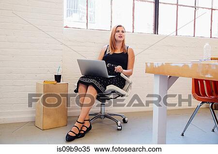 Woman in office chair using laptop View Large Photo Image Stock Photography - Woman in office chair using laptop. Fotosearch