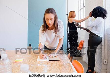 Stock Image - Woman in office writing in notepad. Fotosearch