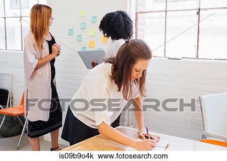 Stock Image - Woman in office writing in notepad. Fotosearch