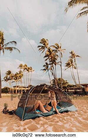 Stock Image - Woman in tent on sandy beach, Princeville, Hawaii, US. Fotosearch