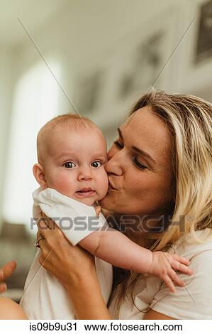 Stock Image - Woman kissing baby daughter on cheek. Fotosearch