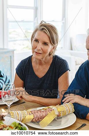 Picture - Woman listening attentively at dining table in home party. Fotosearch