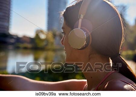 Stock Image - Woman listening to music with headphones in city park. Fotosearch