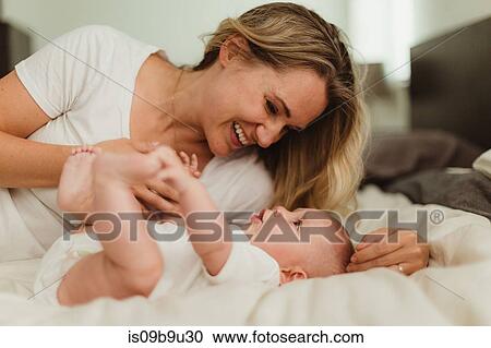 Stock Image - Woman lying on bed playing with baby daughter. Fotosearch