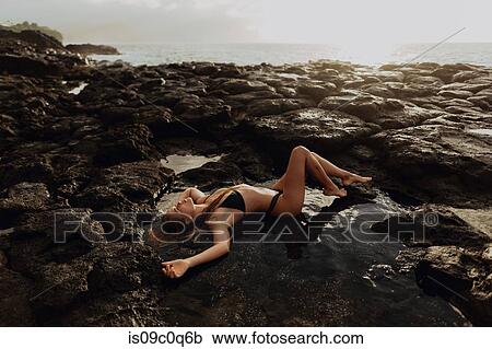 Woman lying on rocks by seaside, Princeville, Hawaii, US View Large Photo Image Stock Image - Woman lying on rocks by seaside, Princeville, Hawaii, US. Fotosearch