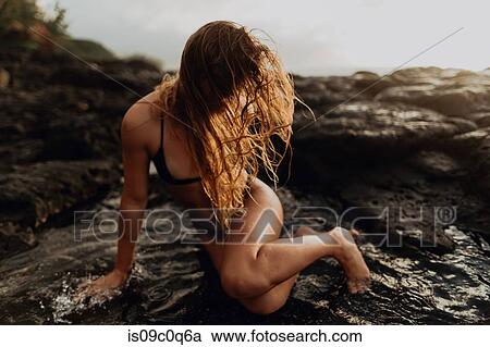 Stock Image - Woman posing on rocks by sea, Princeville, Hawaii, US. Fotosearch