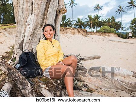 Stock Image - Woman relaxing by old tree trunk, Kailua Beach, Oahu, Hawaii. Fotosearch