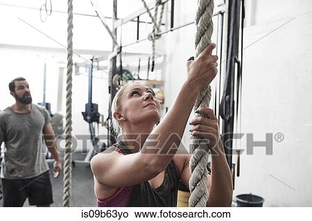 Picture - Woman rope climbing in cross training gym. Fotosearch