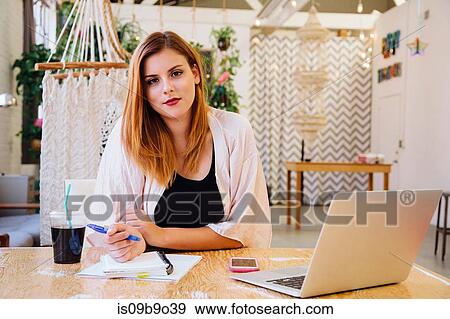 Stock Photo - Woman sitting at desk in creative studio looking at camera smiling. Fotosearch