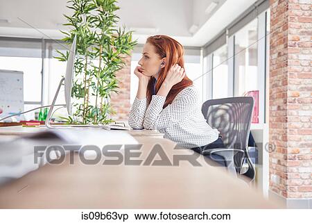 Stock Photography - Woman sitting at desk looking away. Fotosearch