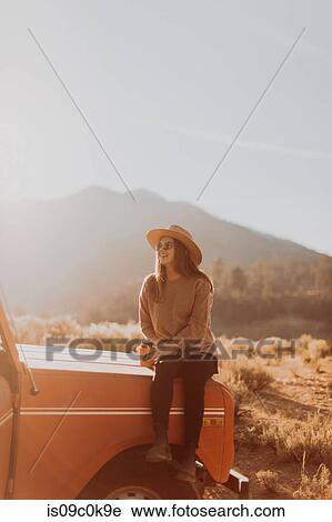 Stock Image - Woman sitting on bonnet of off road vehicle, Kennedy Meadows, California, US. Fotosearch