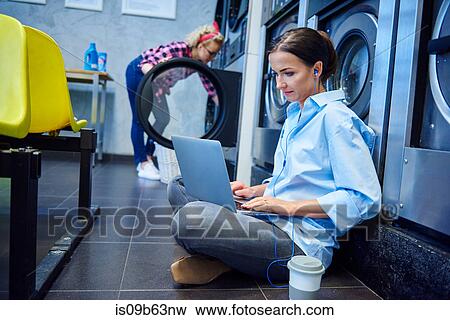 Woman sitting on laundrette floor typing on laptop View Large Photo Image Stock Photo - Woman sitting on laundrette floor typing on laptop. Fotosearch