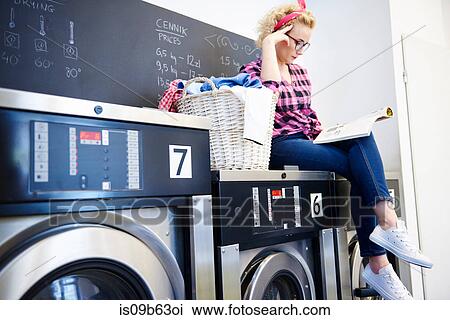 Woman sitting on top of washing machine reading magazine at laundrette View Large Photo Image Stock Image - Woman sitting on top of washing machine reading magazine at laundrette. Fotosearch