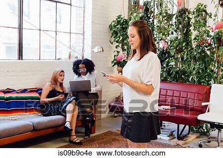 Stock Image - Woman standing in office texting on smartphone. Fotosearch