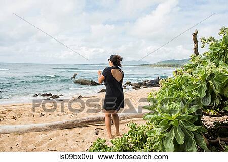 Stock Photograph - Woman taking photo on Kapaa Beach, Kauai, Hawaii. Fotosearch