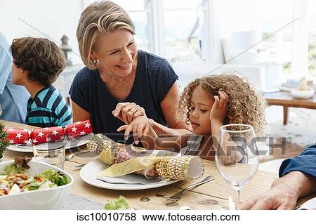 Woman talking to granddaughter playing with Christmas cracker at dining table View Large Photo Image Stock Photo - Woman talking to granddaughter playing with Christmas cracker at dining table. Fotosearch