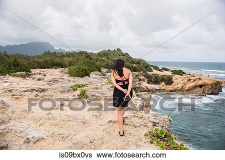 Stock Photograph - Woman walking with cellphone in hand, Shipwreck Beach, Kauai, Hawaii. Fotosearch