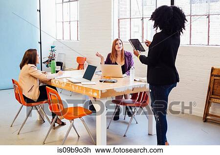 Stock Image - Woman with digital tablet speaking to colleagues working at desk. Fotosearch
