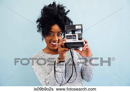 Stock Photograph - Woman with instant camera looking at camera smiling. Fotosearch