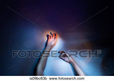Stock Image - Woman's arms and hands raised, cropped low key studio shot. Fotosearch