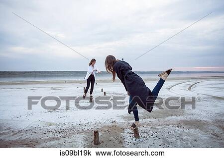 Stock Image - Women balancing on wooden stumps on beach, Odessa, Ukraine. Fotosearch