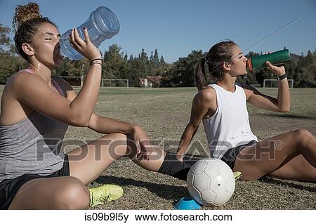 Stock Photo - Women sitting on football pitch drinking from water bottle. Fotosearch