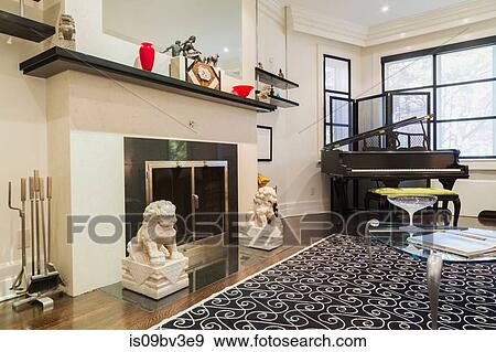 Wood-burning fireplace, grand piano, glass top and silver metal coffee table in living room, wood plank flooring and rug View Large Photo Image Stock Photo - Wood-burning fireplace, grand piano, glass top and silver metal coffee table in living room, wood plank flooring and rug. Fotosearch