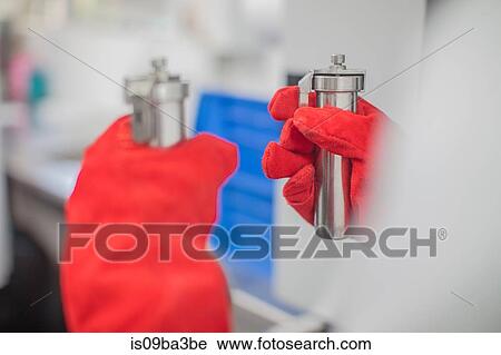 Stock Image - Worker in thread factory, holding beakers of dye, close-up. Fotosearch