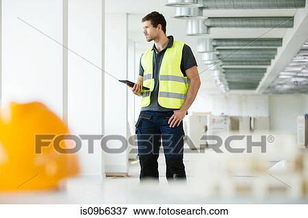 Stock Photo - Workers wearing hi vis vest, standing in newly constructed office space. Fotosearch