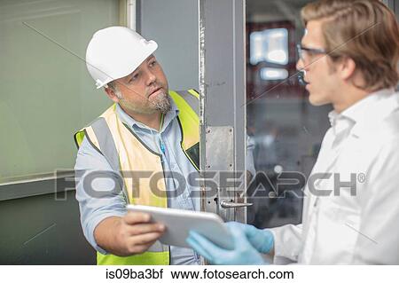 Stock Image - Workman and lab worker in thread factory, holding digital tablet. Fotosearch