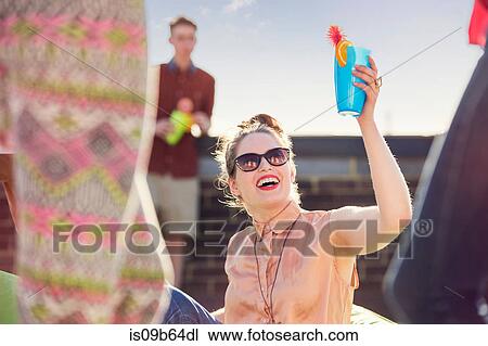 Stock Image - Young adult friends holding up cocktail at roof party in London, UK. Fotosearch