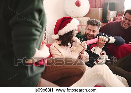 Stock Image - Young adult friends pulling christmas crackers on sofa at christmas party. Fotosearch