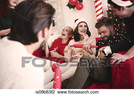 Stock Image - Young adult friends pulling christmas crackers on sofa at christmas party. Fotosearch