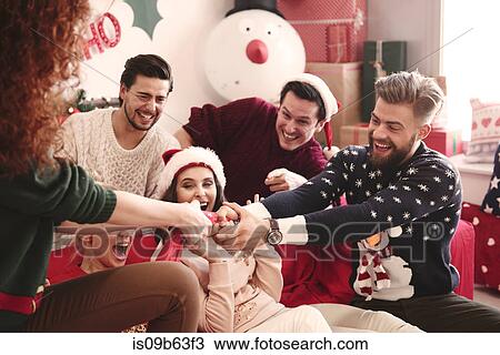 Stock Image - Young adult friends pulling christmas crackers on sofa at christmas party. Fotosearch