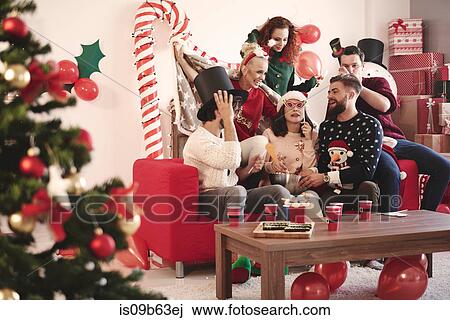 Stock Image - Young adult friends trying on party hats at christmas party. Fotosearch
