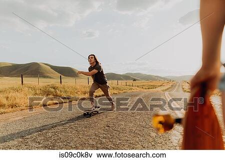 Stock Photo - Young barefoot male skateboarder skateboarding on rural road, girlfriend watching, Exeter, California, USA. Fotosearch