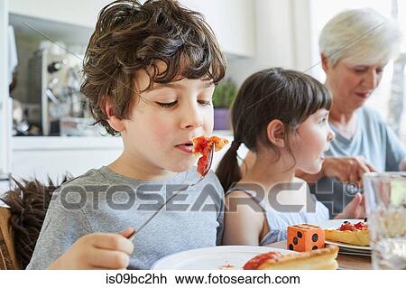 Young boy eating lunch at table with sister and grandmother View Large Photo Image Stock Image - Young boy eating lunch at table with sister and grandmother. Fotosearch
