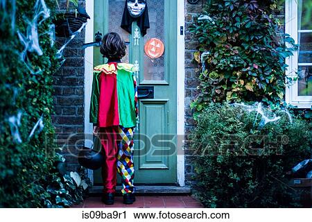 Stock Image - Young boy in halloween costume, standing at door, trick or treating, rear view. Fotosearch