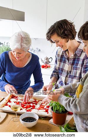 Stock Photo - Young boy, mother and grandmother making pizza together in kitchen. Fotosearch